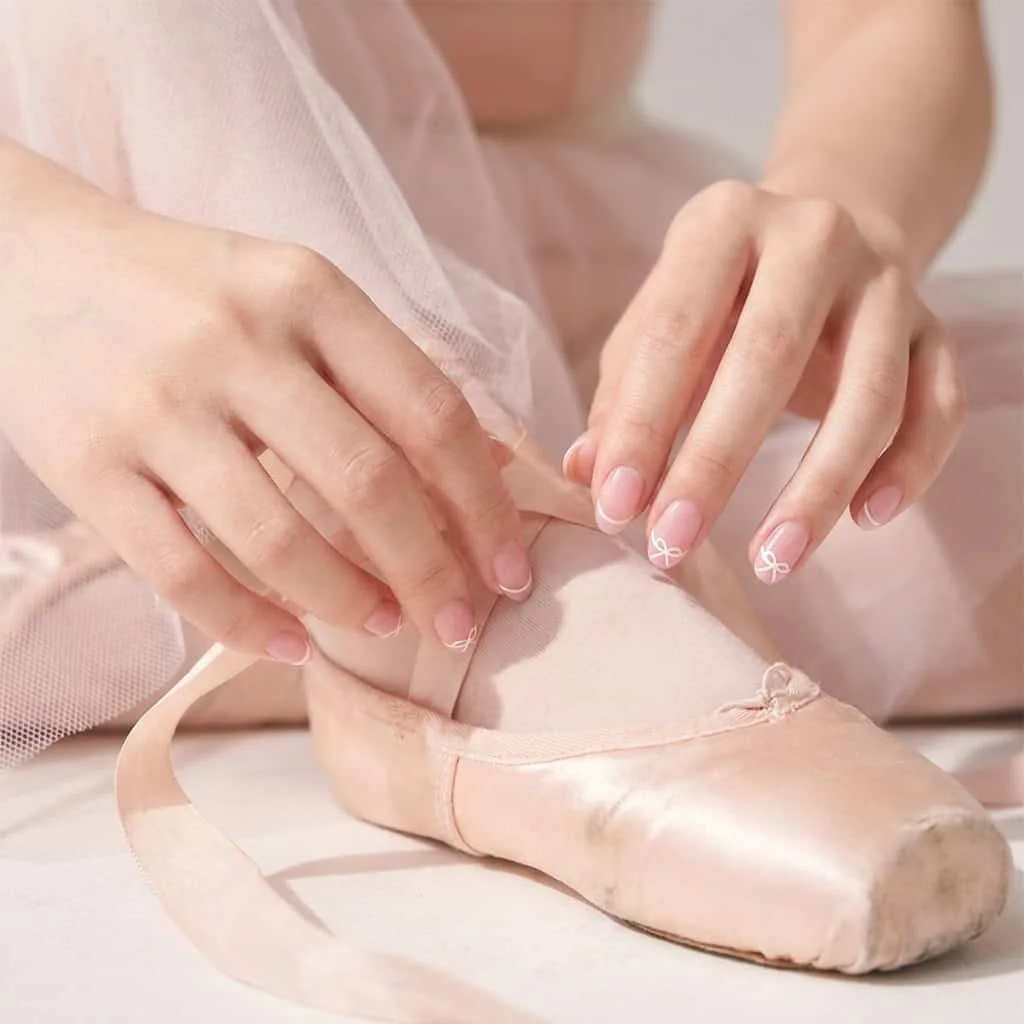 A classic micro-French manicure where the line ties into a small, delicate bow at the center.